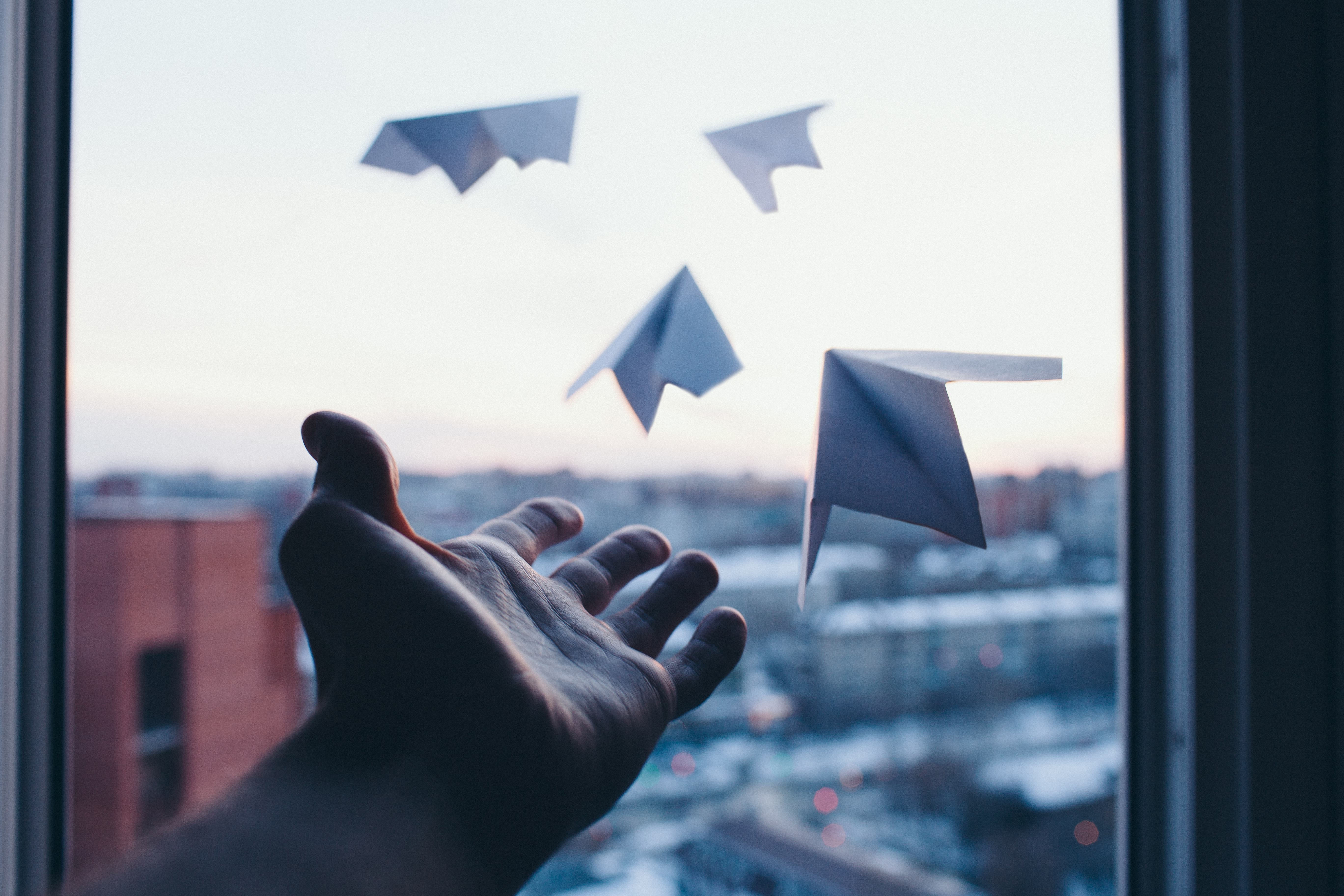 A hand stretched out towards a window with four paper planes flying out of the window