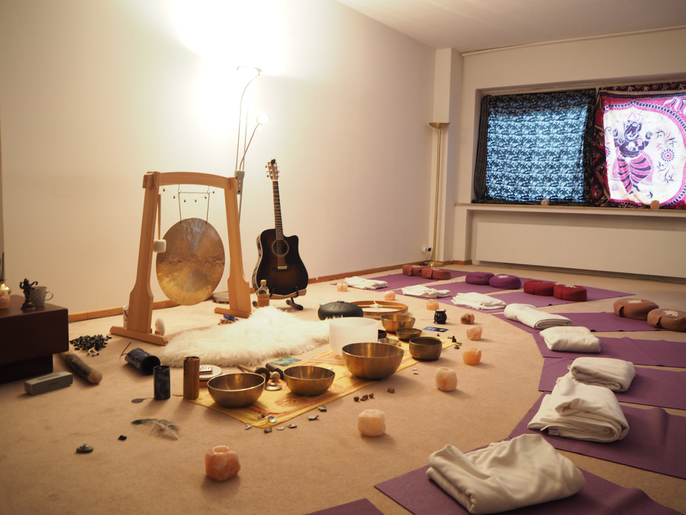 A room set up for sound baths with yoga mats, a guitar, various singing bowls and a gong