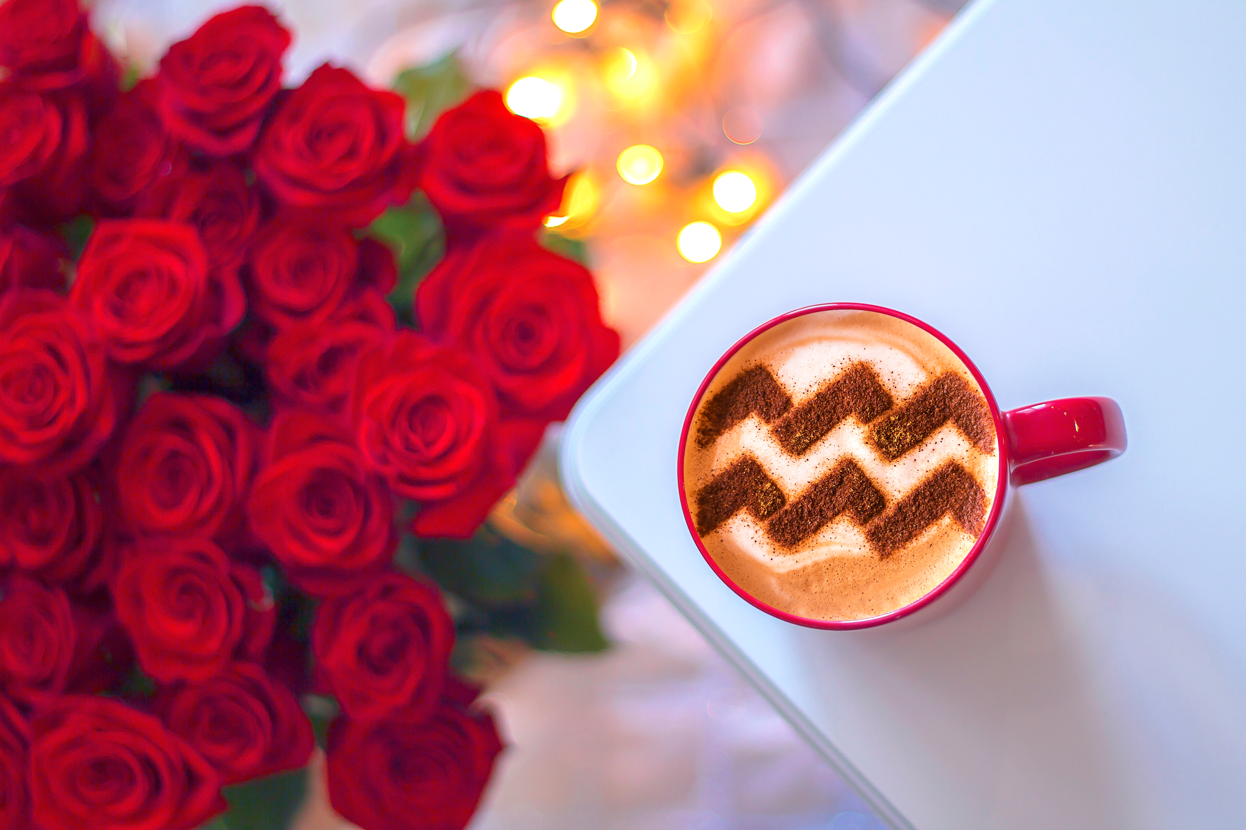 An image of the Aquarius sign in a coffee next to a bunch of red roses