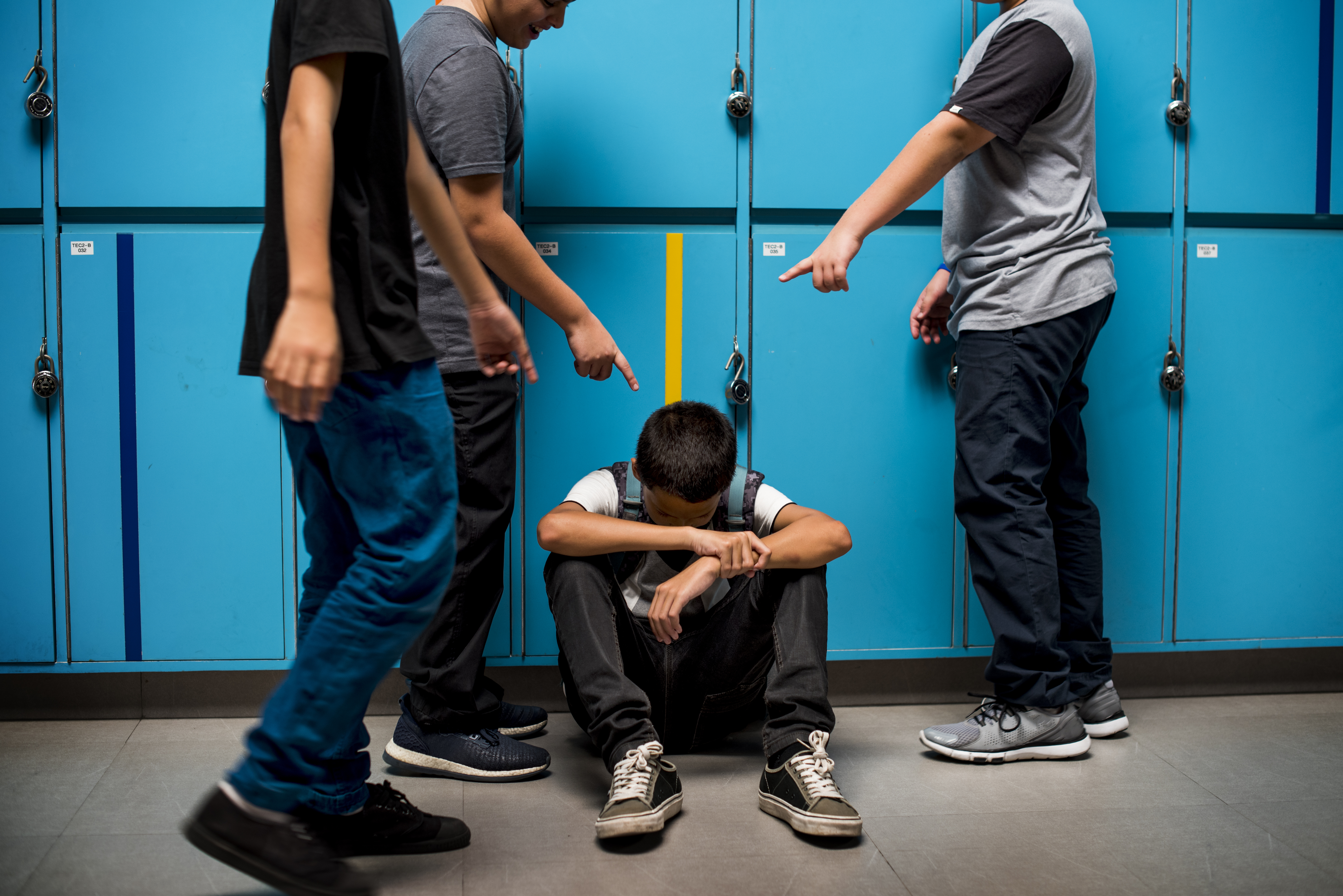 Boy student sat on the floor with three boys stood around him pointing