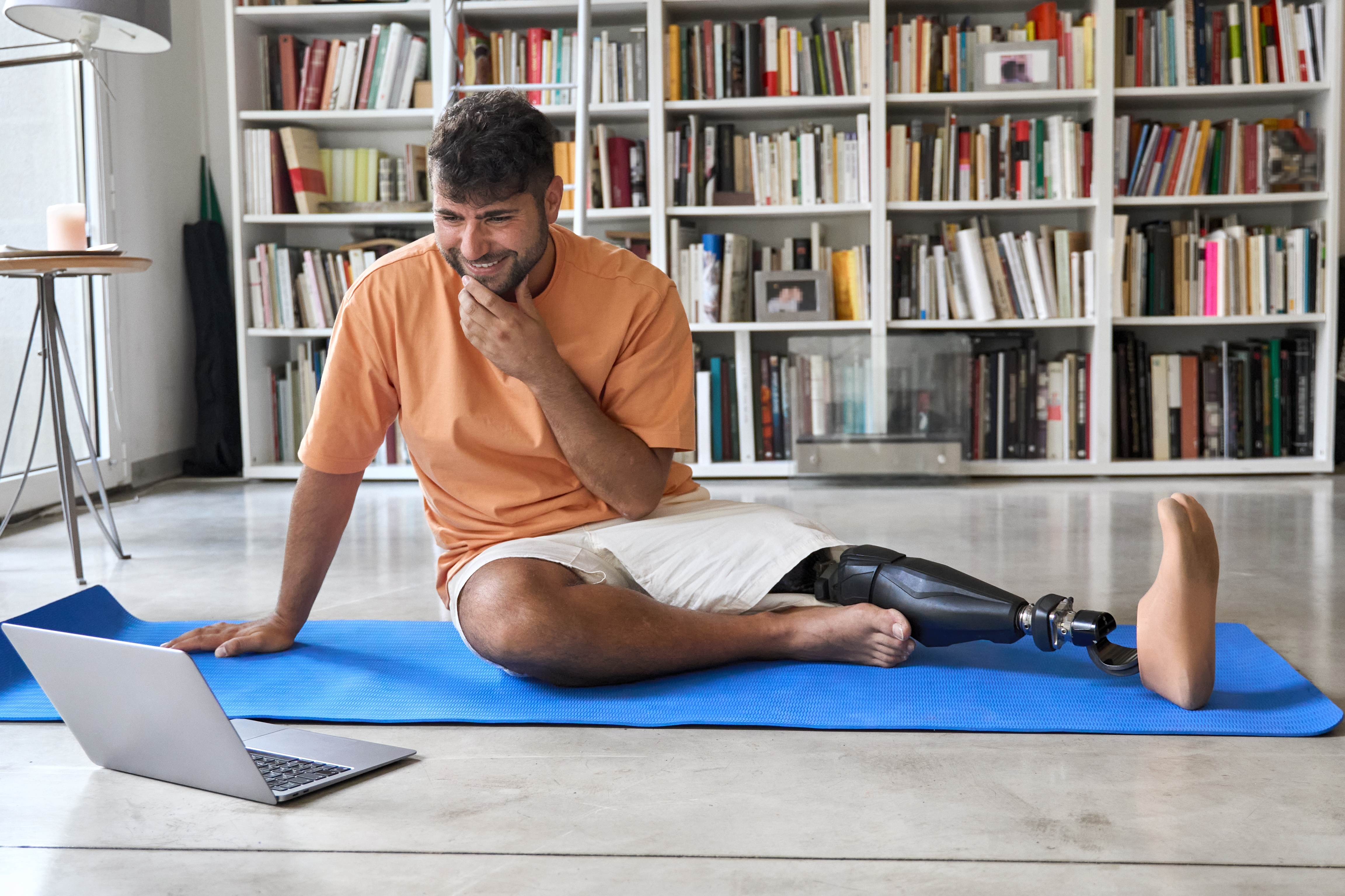 Man sitting on yoga mat smiling at laptop
