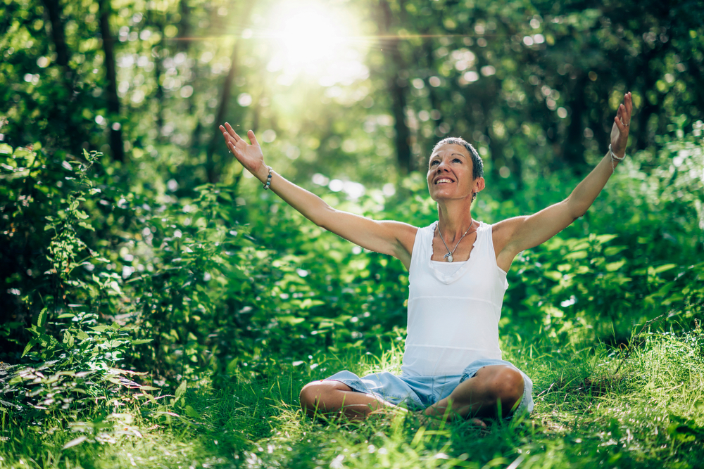 Woman meditating in the woods, smiling with her hands and face up to the sky