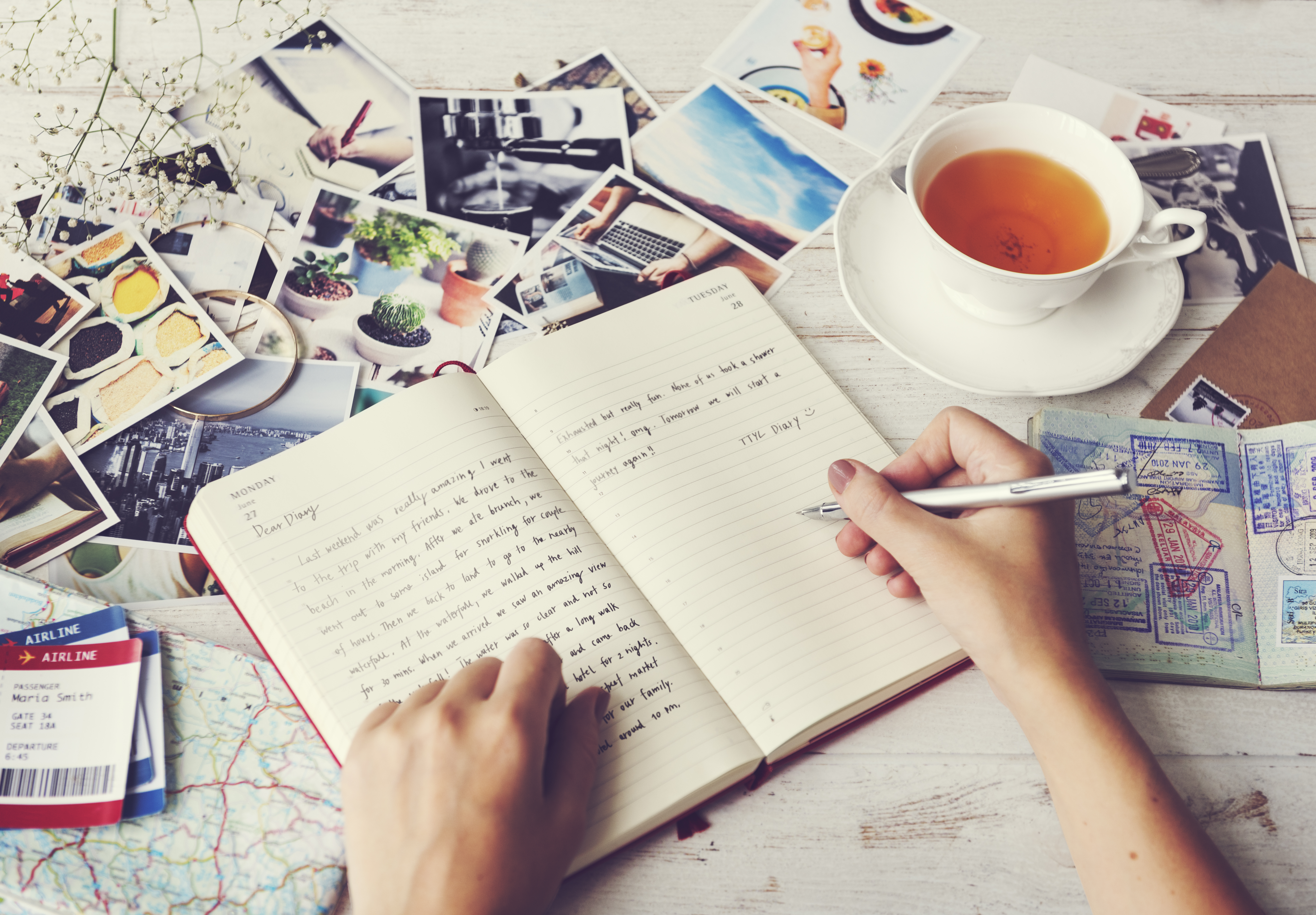 Someone writing in a journal surrounded by printed out pictures and a mug of tea