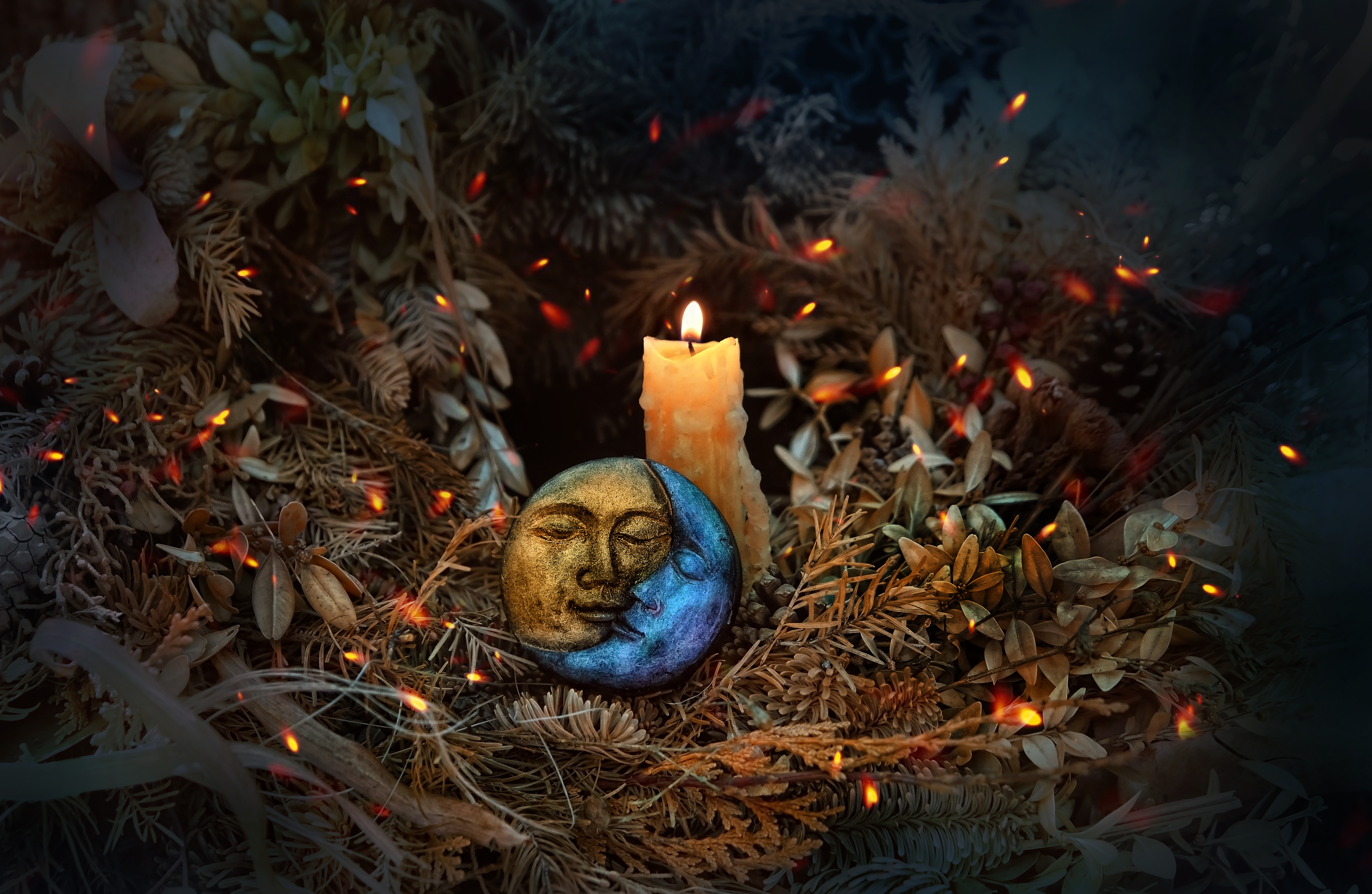 A small figure of a sun and moon entwined surrounded by leaves and a lit candle 
