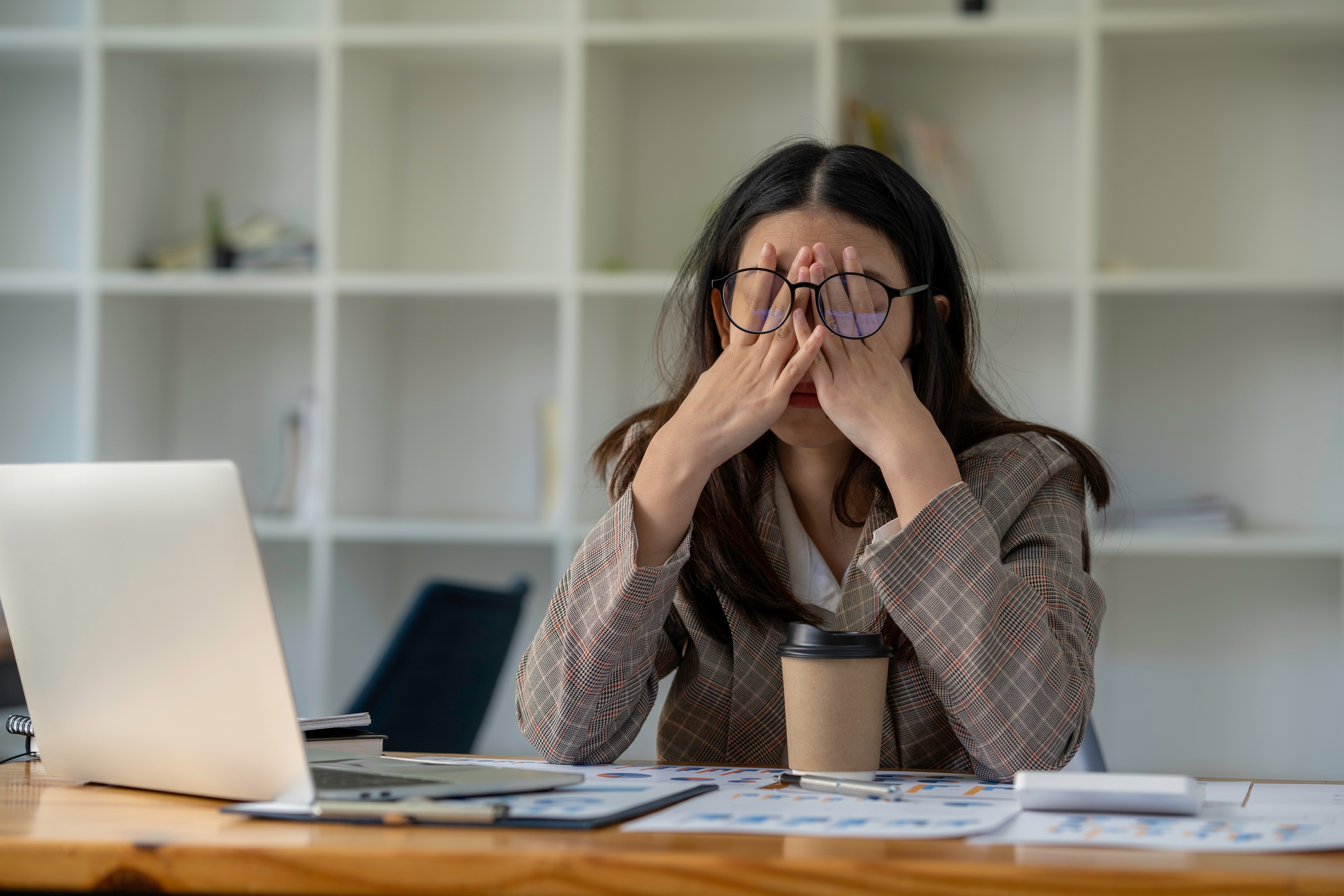 Woman overwhelmed and stressed at her desk, with her face in her hands